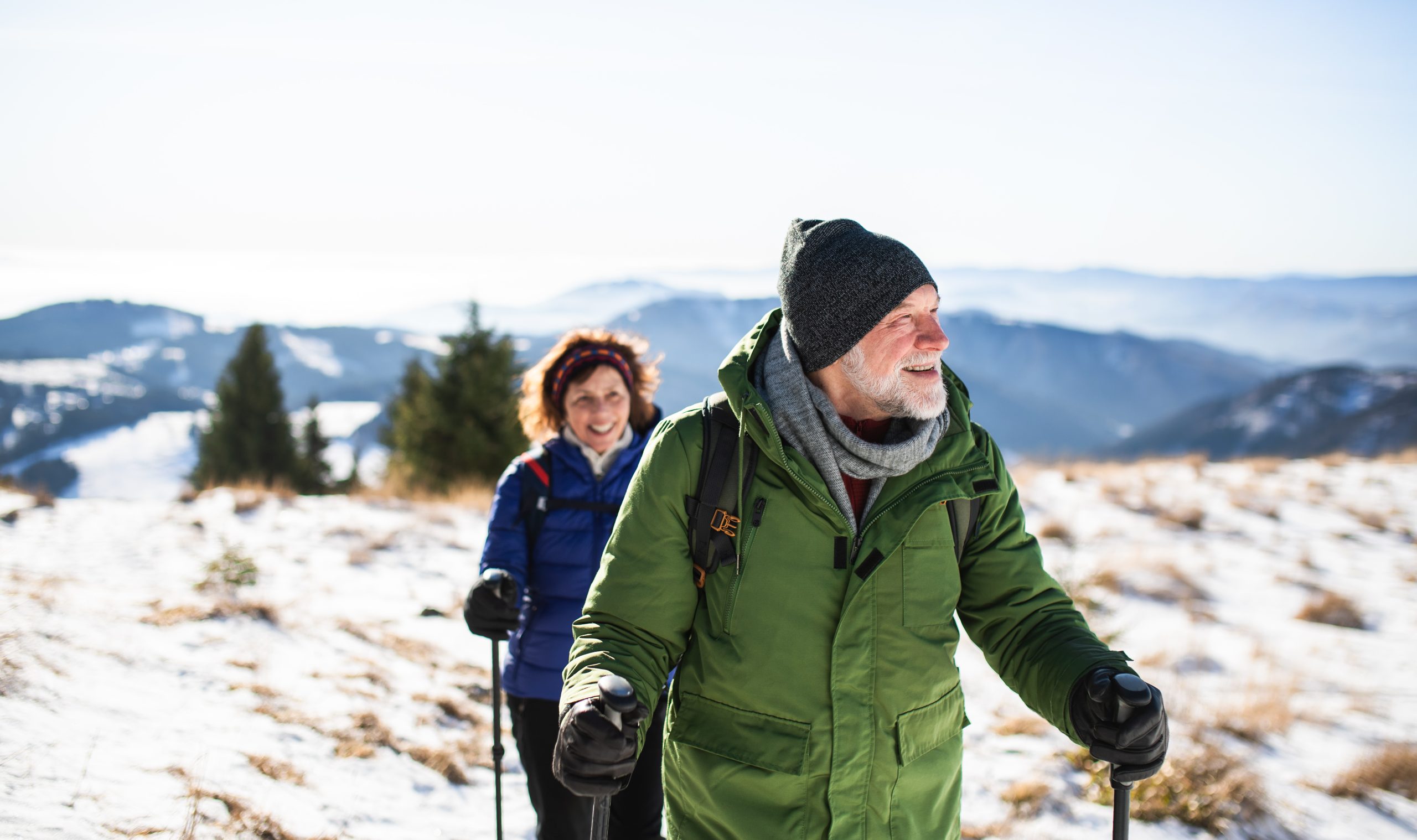 Senior couple with nordic walking poles hiking in snow-covered winter nature.